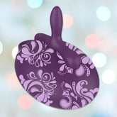 Set against pastel bokeh lights, the Bouncy Bliss Inflatable Seat Vibrator in purple, featuring a handle and floral pattern, discreetly promises an inventive hands-free design with 10 vibration modes for seamless enjoyment and elegance.